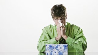 A stock image of a man blowing his nose in a tissue paper.