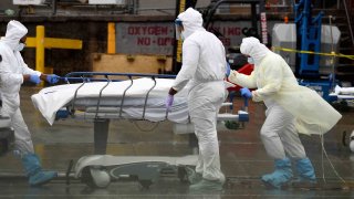 In this April 9, 2020, file photo, medical personnel move a deceased patient to a refrigerated truck serving as make shift morgues at Brooklyn Hospital Center in New York City.