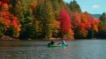 Two people and a dog canoe in Waterbury, Vermont, as the trees change colors in the fall