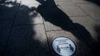 A person casts a shadow while walking by a social distancing sign in the National Gallery of Art Sculpture Garden in Washington, D.C., amid the coronavirus pandemic, Oct. 20, 2020.