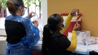 Two women, both in masks and one in a gown, prepare doses of the covid vaccine