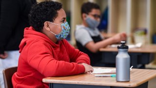 Students sit at their desks while wearing face masks.