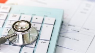 A photo of a stethescope on top of a calculator and medical bills.