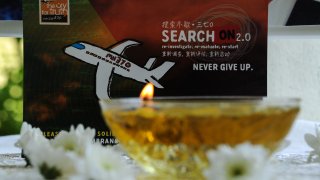 FILE - A candle burns a prayer message for passengers of missing Malaysia Airlines flight MH370