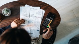 Overhead view of young Asian woman managing personal banking and finance at home. Planning budget and calculating expenses while checking her bills with calculator. Managing taxes and financial bills. Home budgeting. Concept of finance and economy