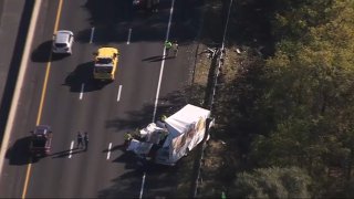 A white tractor-trailer sits damaged on the right side of a highway