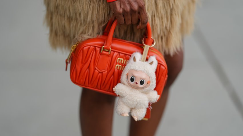 COPENHAGEN, DENMARK – AUGUST 07: A guest wears a tan long-fringe mini skirt, and carries an orange Miu Miu quilted leather mini bag with rolled top handles, gold-tone hardware and a top-zip closure, accented by a cream plush Labubu doll bag charm in a fuzzy hooded outfit with ears hanging from a gold ring, outside Birrot, during Copenhagen Fashion Week, on August 07, 2025 in Copenhagen, Denmark (Photo by Edward Berthelot/Getty Images)
